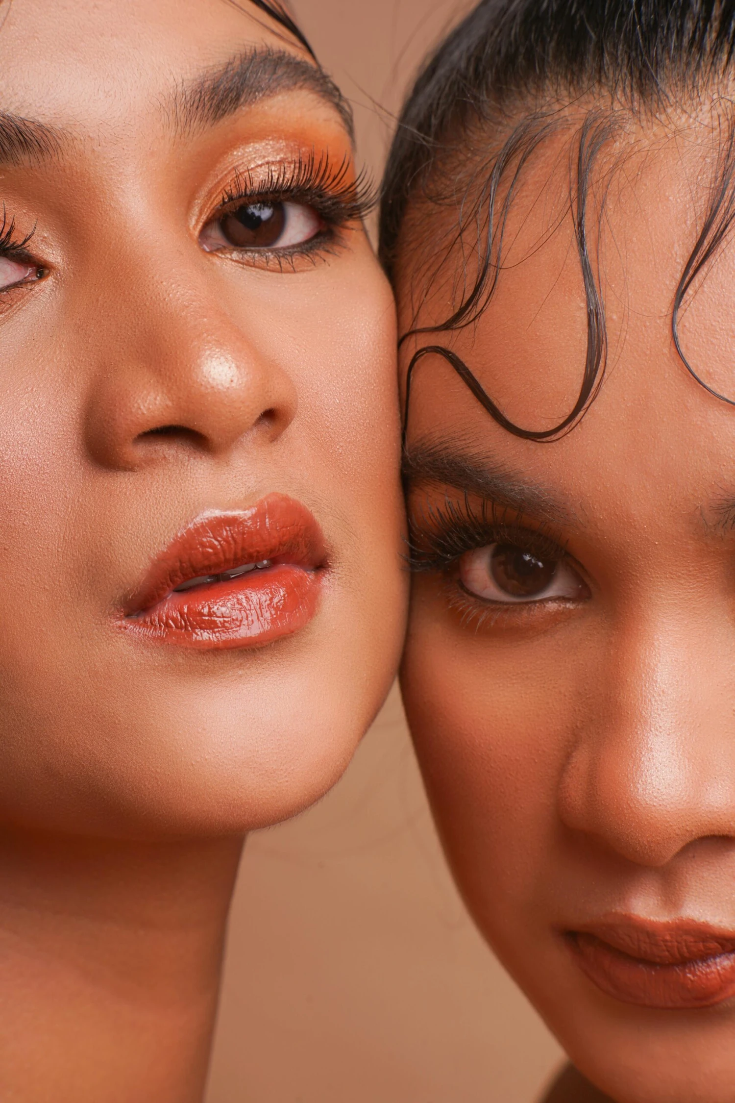 Intimate close-up of two women with striking eye makeup and lipstick.